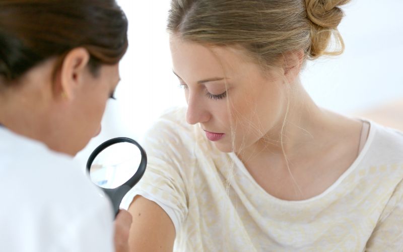 dermatolog ogląda skórę kobiety przez lupę